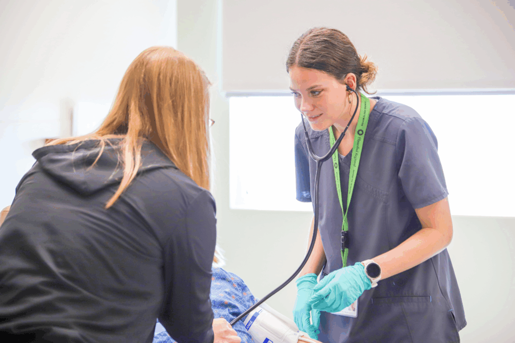 A young healthcare professional in scrubs and gloves listens to a patient's heartbeat with a stethoscope, exuding care and attentiveness in a bright clinic.