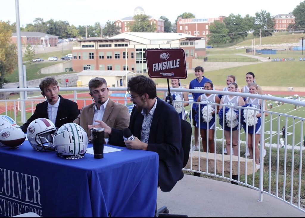 Students sitting at a sport commentating table.