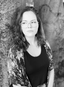An image of a woman leaning against a tree. 